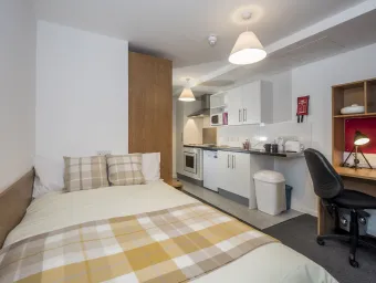 A modern studio flat showing bed, desk and kitchenette.