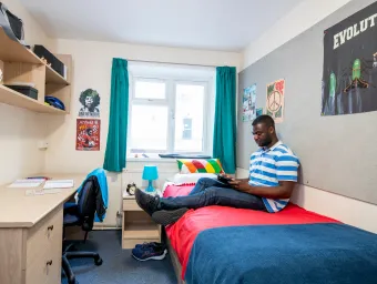 Student sat on bed, working on tablet computer.