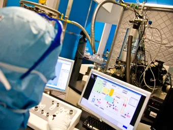 A researcher analysing a complex electrical circuit on a monitor in a cleanroom.