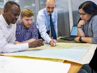A Southampton Geospatial project team meets, with one researcher standing up, pointing to a map that his colleagues are gathered around