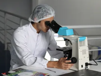 A researcher in a white lab coat looks through a microscope.