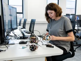 A researcher sits at a desk, assembling electronic components