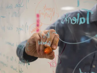 Close up of someone's hand as arm as they write in felt tip on a transparent board