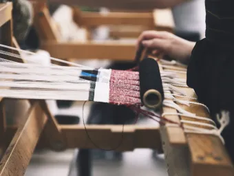 Close up of someone working at a loom. You can only see the person's hands as they work the thread.