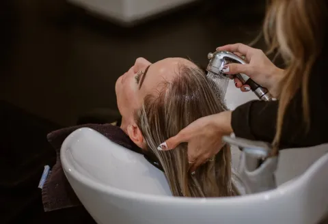 A hairdresser washes a client's hair at a basin