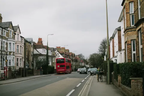 A road with a red bus, a cyclist pushing a bike, a pedestrian and cars