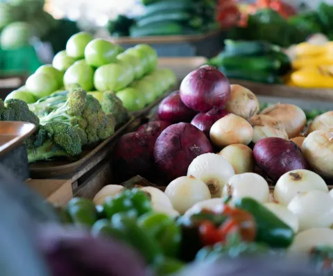 Assorted vegetables including onions, bell peppers, broccoli, and beetroot on a market stand.