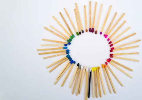 Circle of multicolored matchstick tips arranged in a rainbow gradient on a white background, creating a radial pattern.