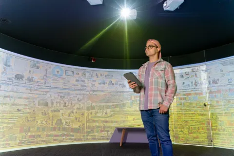 Person stands in front of a 180-degrees curved screen, which is displaying a historic painting