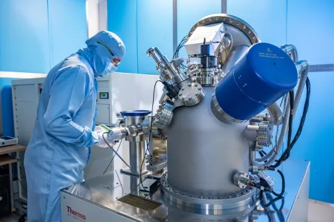 A man in full cleanroom uniform is working with equipment