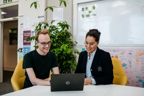 James Baker and Ammandeep K Mahal are in an office, smiling and looking at a laptop screen together.