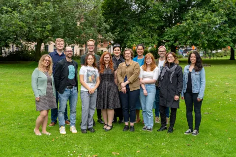 A group of people are standing in a park.They are smiling happily at the camera.