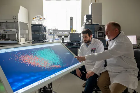 Two scientists observing blood test results on a screen. The results are colour coded in red and blue to show whether cancer is present or not.