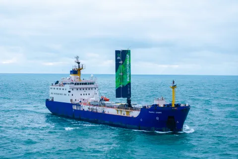 A large cargo vessel sailing on the ocean. It has a 20 metre-high wing sail. 