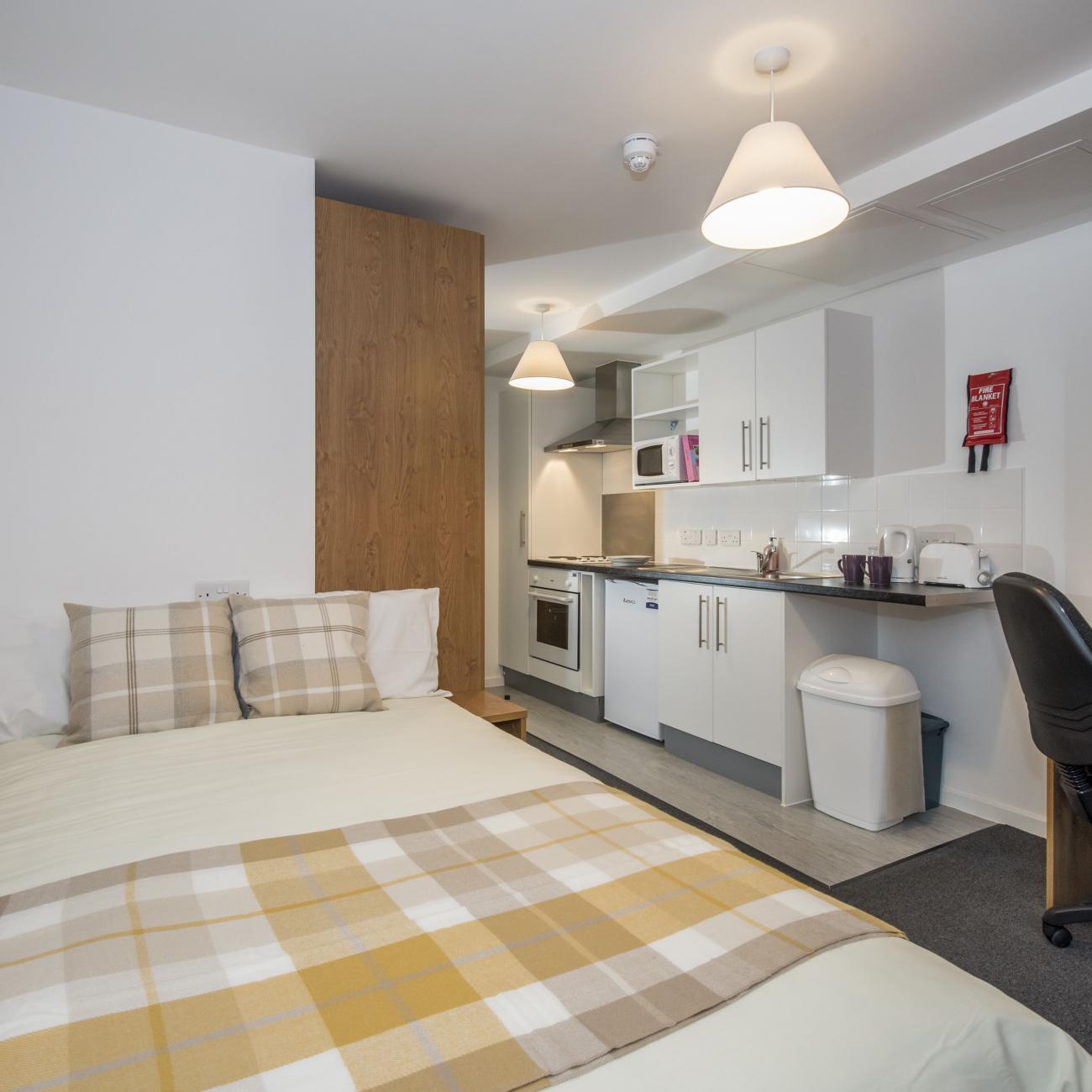 A modern studio flat showing bed, desk and kitchenette.