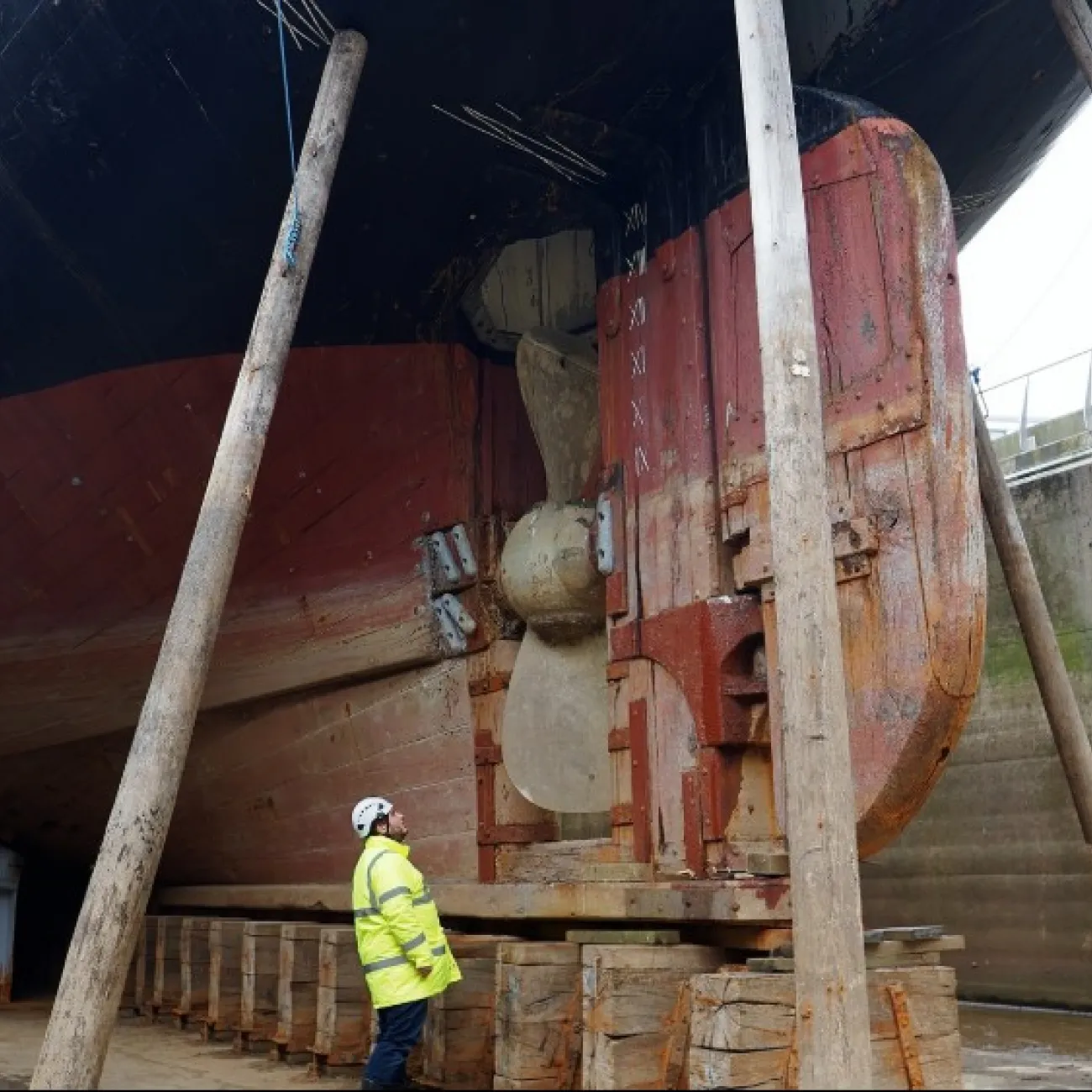 A worker in a high-viz jacket examines the massive hull of the RRS Discovery