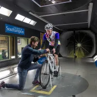 Man on bike in wind tunnel with man adjusting his wheel.