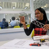 Civil engineering student Virtue, a young Black woman, works on a design at a desk in our campus building, immersed in her work