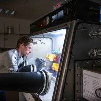 A researcher wearing safety goggles works with chemicals in a glovebox