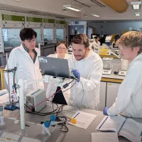 A group of students near the open laptop in the laboratory