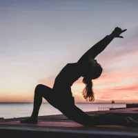 Silhouette of a person doing yoga by the water at sunset.