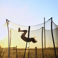 Child performing a flip on a trampoline during sunset in a field.