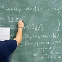 A student writing a complex mathematical equation on a blackboard