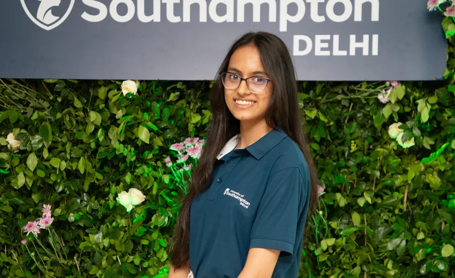 An Indian student stood in front of a University of Southampton Delhi sign, which has been mounted on a living wall.